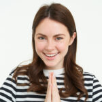 portrait of woman showing namaste gesture, holding palms clenched together near chest, standing isolated over white background
